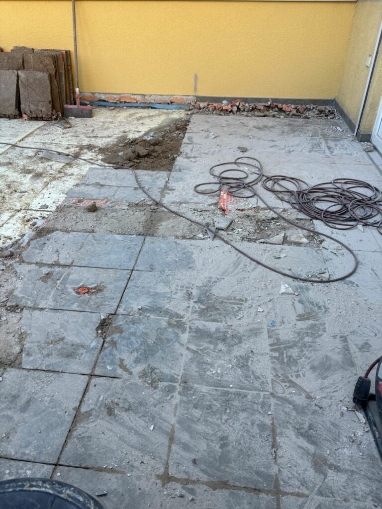 Detail der laufenden Arbeiten auf der Dachterrasse: Fliesen gelöst, Randzone aufgestemmt, Schutt sowie Kabel/Maschine im Arbeitsbereich – Schritt zur Untergrund‑ und Abdichtungserneuerung.