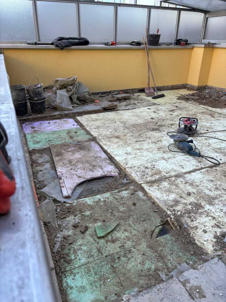 Baustelle auf der Dachterrasse: Fliesen und Aufbau teilweise entfernt, Untergrund freigelegt; Schutt, Kabel und Schleif/Trennwerkzeuge – Schritt zur Erneuerung von Bodenaufbau und Abdichtung.